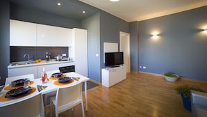 A modern kitchen with white cabinets, a dining table set for four, and a flat-screen TV mounted above the counter. - Aurum ApartHotels Gambara (Milan)