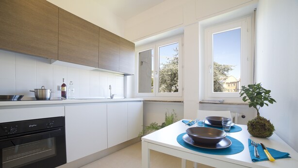 A modern kitchen with white cabinets, a built-in oven, and a dining area with a table set for two. - Aurum ApartHotels Gambara (Milan)