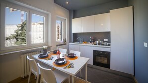 A modern kitchen with white cabinets, a built-in oven, and a dining area with a white table set for two. - Aurum ApartHotels Gambara (Milan)