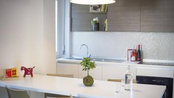 Una cocina moderna con encimera blanca, un lavamanos, una planta en maceta y una botella de vino.