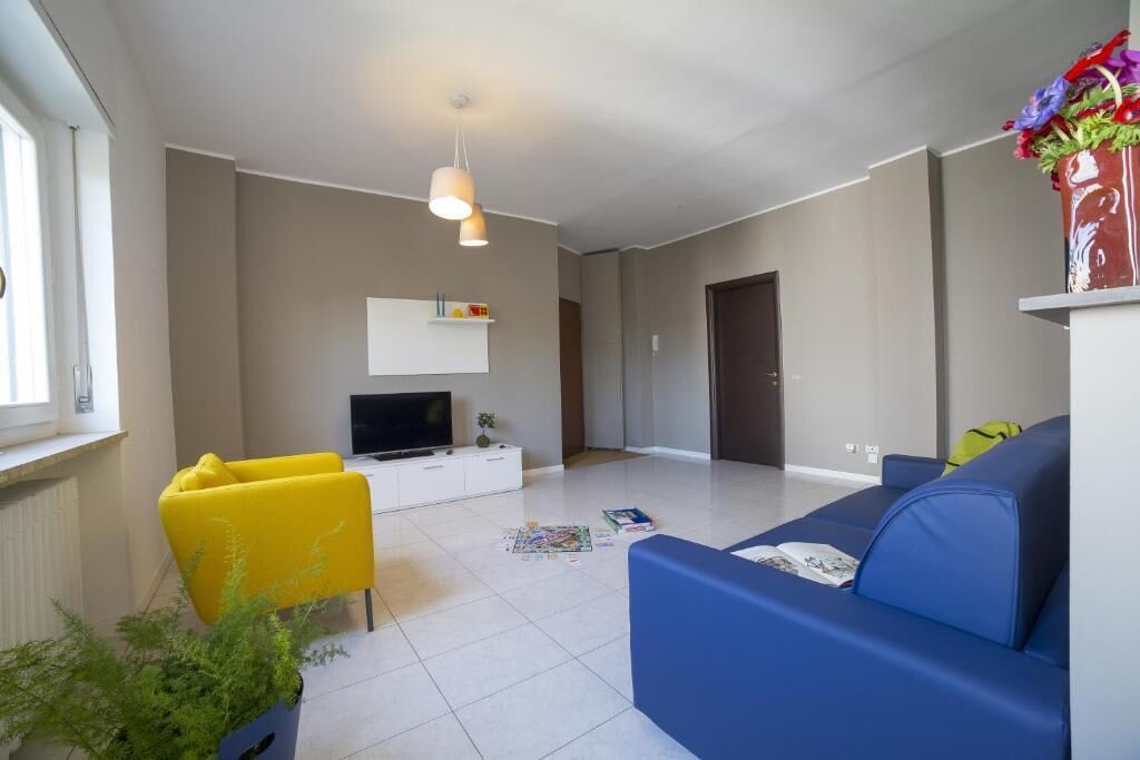 Ein Wohnzimmer mit einer Couch, einem gelben Sessel, einem Fernseher, einem weißen Schrank und einer Pflanze.