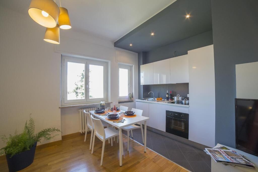 A modern kitchen with white cabinets, a dining table with chairs, and a potted plant.