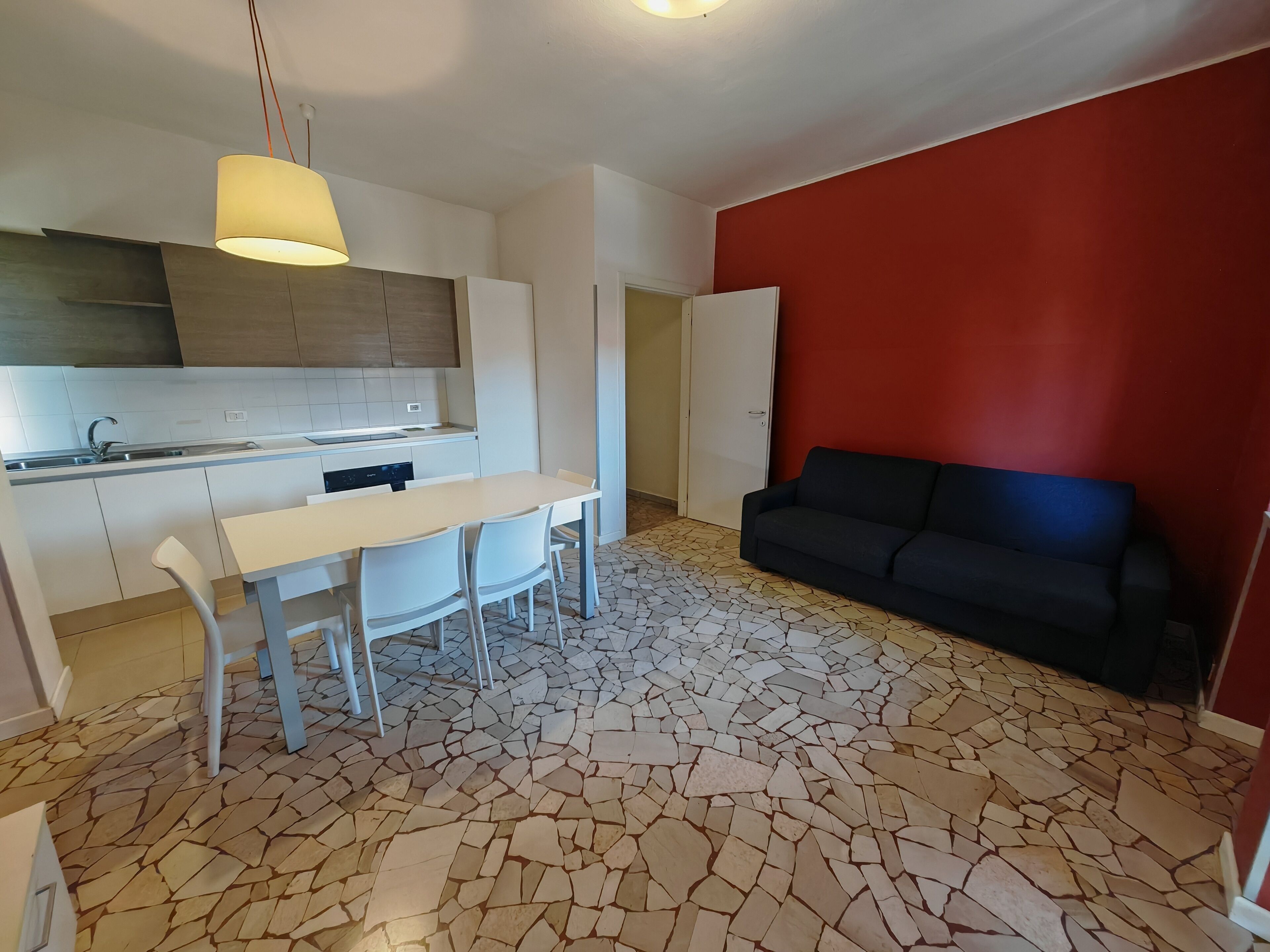 A compact living space with a kitchenette, a dining area with chairs, a sofa, and a tiled floor.