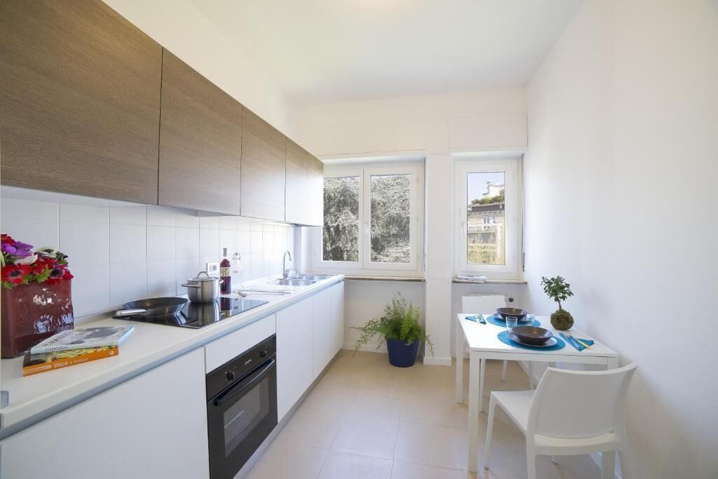 Una cocina moderna con armarios blancos, horno empotrado y comedor con mesa y sillas blancas.