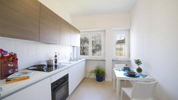 Una cocina moderna con armarios blancos, horno empotrado y comedor con mesa y sillas blancas.