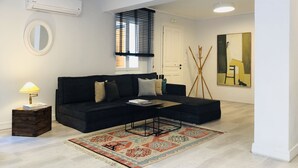 A modern living room with a black sofa, a patterned rug, a standing lamp, and a large abstract painting. - SV Acropolis Residence (Athens)