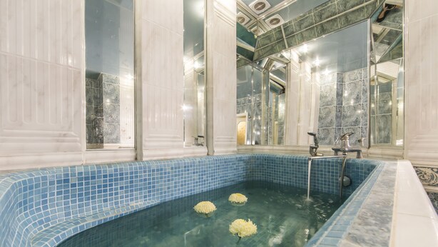 A large indoor swimming pool with blue mosaic tiles, clear water, and three white flowers floating. - Stylish Apartment Close ot the Opera (Kyiv)