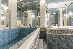 Un baño lujoso con una bañera de azulejos azules, un tocador de mármol y un espejo grande.