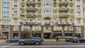 A multi-story building with balconies, storefronts, and parked cars. - Stylish Apartment Close ot the Opera (Kyiv)