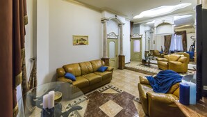A spacious living room with a brown leather sofa, a glass coffee table, and a blue blanket on a brown leather chair. - Stylish Apartment Close ot the Opera (Kyiv)