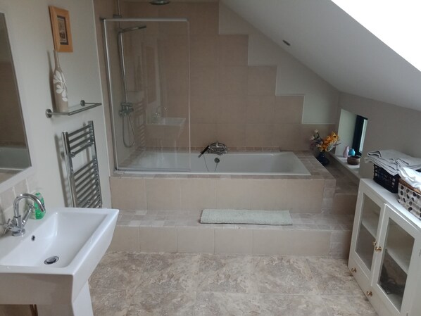 A bathroom with a bathtub, shower, sink, and a small shelf with toiletries. - 2 bed accommodation sleeps 4/5 (Quin)