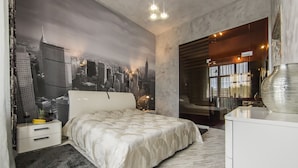 Een slaapkamer met een stadsgezicht muurschildering, een bed met een wit hoofdeinde, een nachtkastje, een grote spiegel en een moderne lamp.