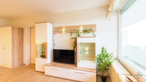 Cozy living room with a fireplace, flat-screen TV, and a cabinet, offering a view of the outside.