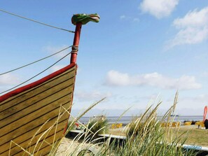 A wooden boat with a red stripe and a green dragon head ornament, docked at a beach with yellow chairs and a view of the sea.