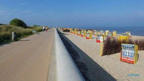 Eine Küstenstraße mit Strandhäusern von der Nummer 20 bis 59, ein Sandstrand und das Meer im Hintergrund.