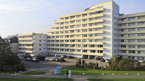 Ein mehrgeschossiges Hotel mit schlichter Fassade, zahlreichen Balkonen und einem Parkplatz davor.