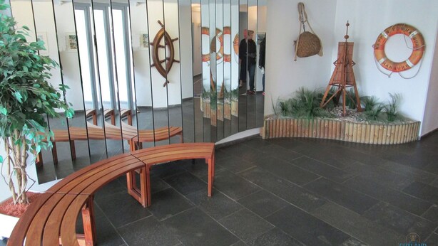 Eine Lobby mit einer gebogenen Holzbank, einem Schiffsschwester, einem Rettungsreifen und einem Modell des Eiffelturms.