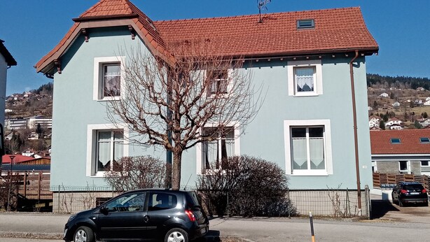 A two-story building with a red-tiled roof and a light blue exterior.