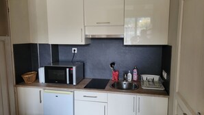 A compact kitchen with white cabinets, a microwave, a sink, and a small refrigerator.