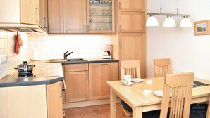 A modern kitchen with wooden cabinets, a dining table with chairs, and a coffee maker. - Rubin apartment 2 - Quiet vacation apartment near the Döser sandy beach (Cuxhaven)