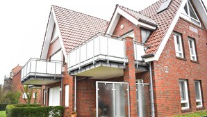 A two-story brick house with a red-tiled roof, a balcony, and a garage door. - Rubin apartment 2 - Quiet vacation apartment near the Döser sandy beach (Cuxhaven)