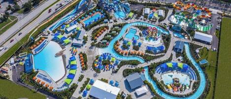 An aerial view of a water park with multiple pools, slides, and a large parking area.