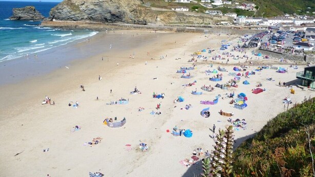 A beach with tents and people, a rocky cliff, and houses in the background. - 4~Short walk~Beach~Pubs~Shops: Chlorine safe Pool and Hot tub, Games room, WiFi  (Portreath)