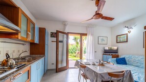 A compact kitchen with wooden cabinets, a gas stove, and a dining area with a table and chairs. - Villa Fiorita (San Teodoro)