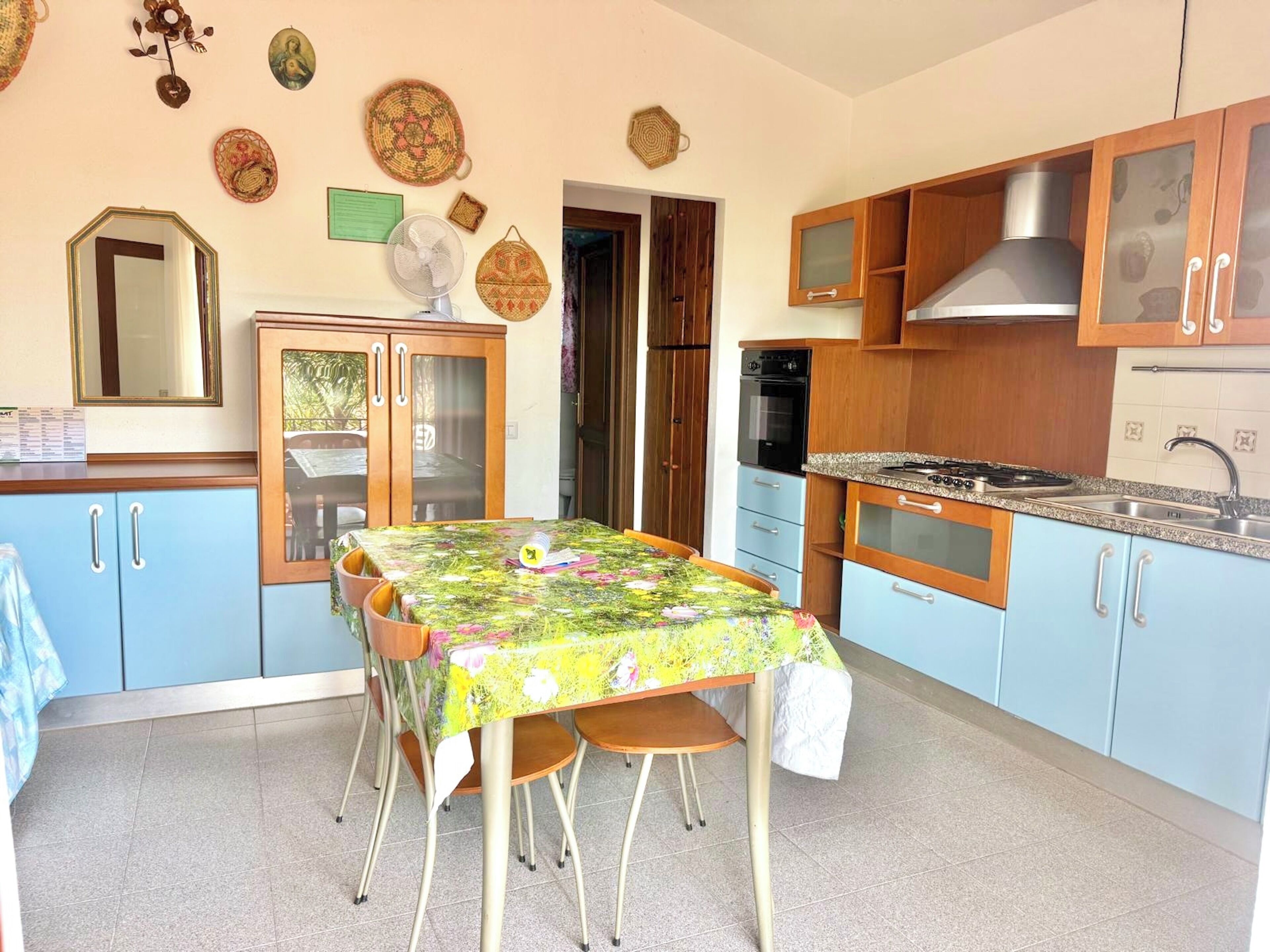 A compact kitchen with a dining area, wooden cabinets, a stove, and a fan.