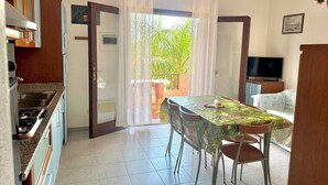A compact kitchen with a dining area, a TV, and a balcony with a view of greenery. - Villa Fiorita (San Teodoro)