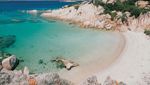A coastal landscape with clear turquoise waters, a sandy beach, and rocky terrain. - Villa Fiorita (San Teodoro)