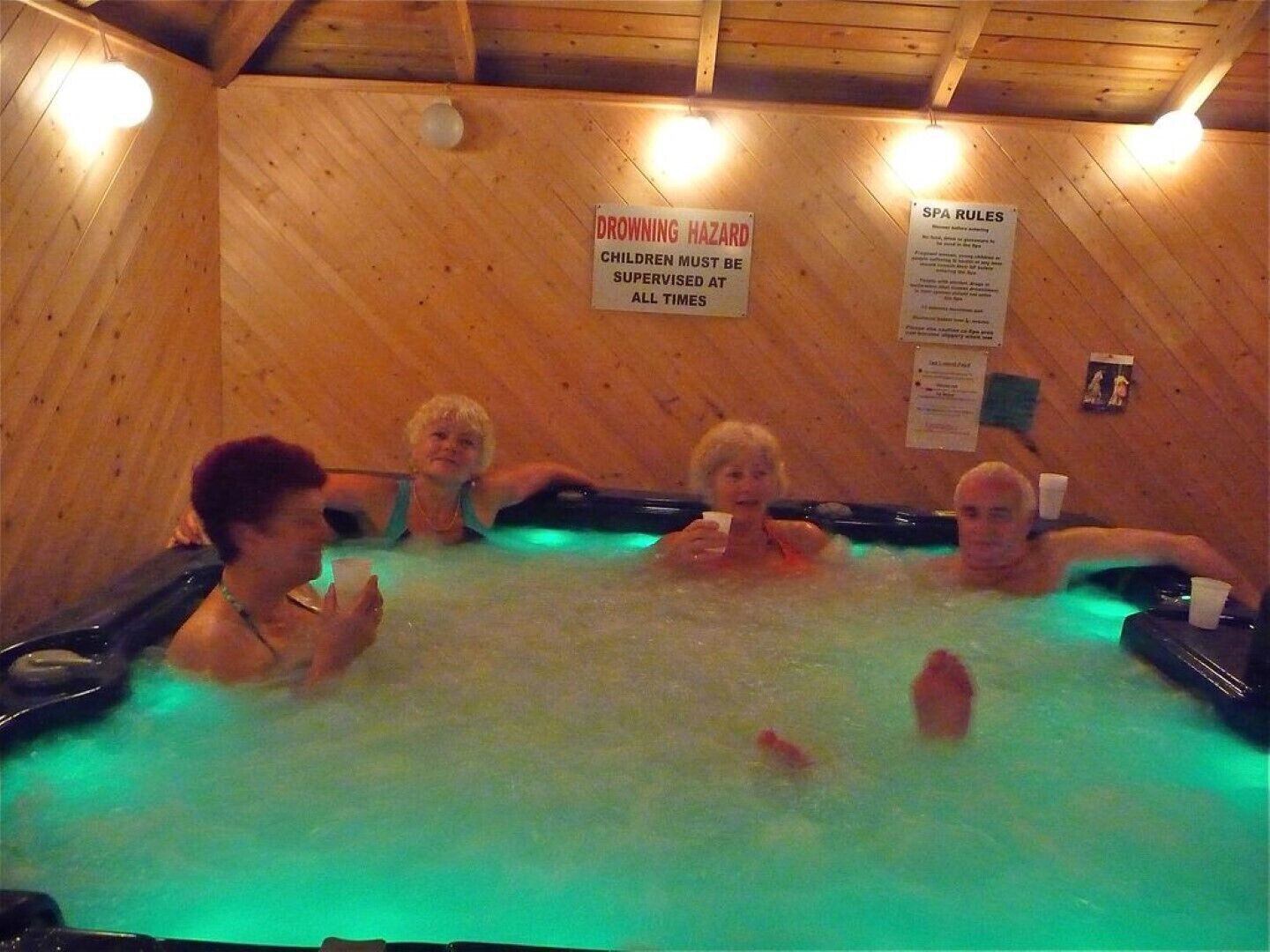 A wooden interior with a hot tub, signs indicating a drowning hazard and spa rules, and a wooden ceiling.