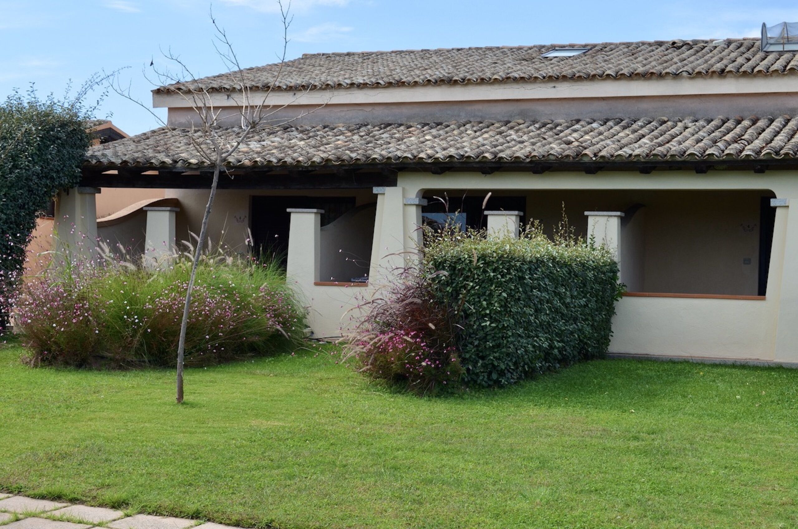 A two-story building with a tiled roof, a small garden with flowering plants, and a clear sky.