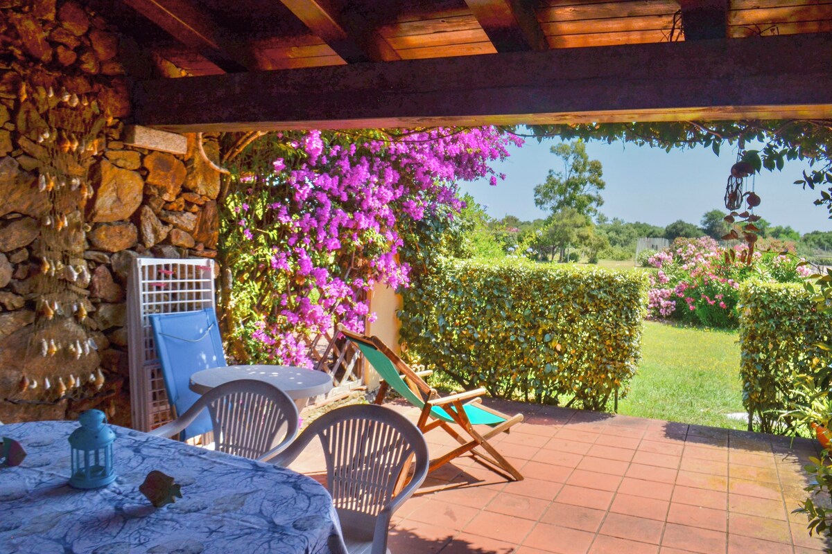 A patio with a table and chairs, a stone wall, and a view of a garden with pink flowers.