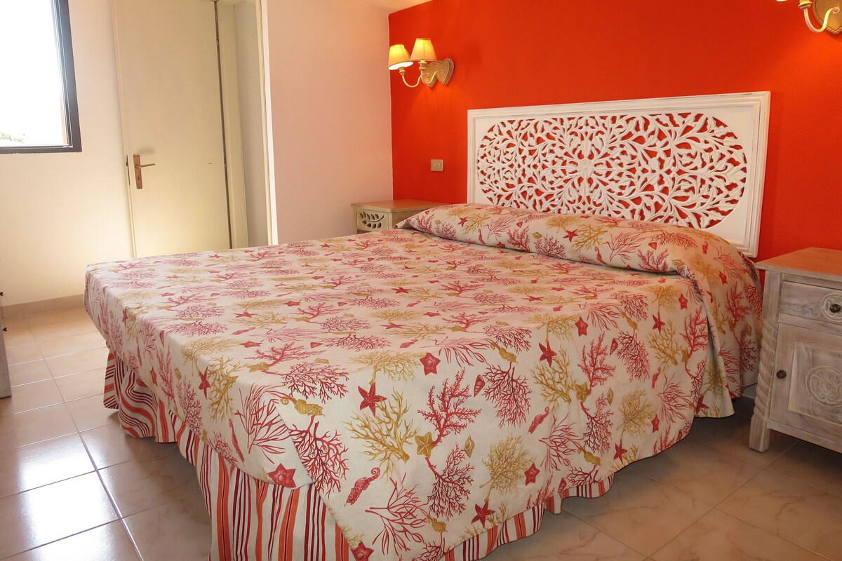 A bedroom with a bed, a nightstand, a wall-mounted lamp, and a decorative headboard.