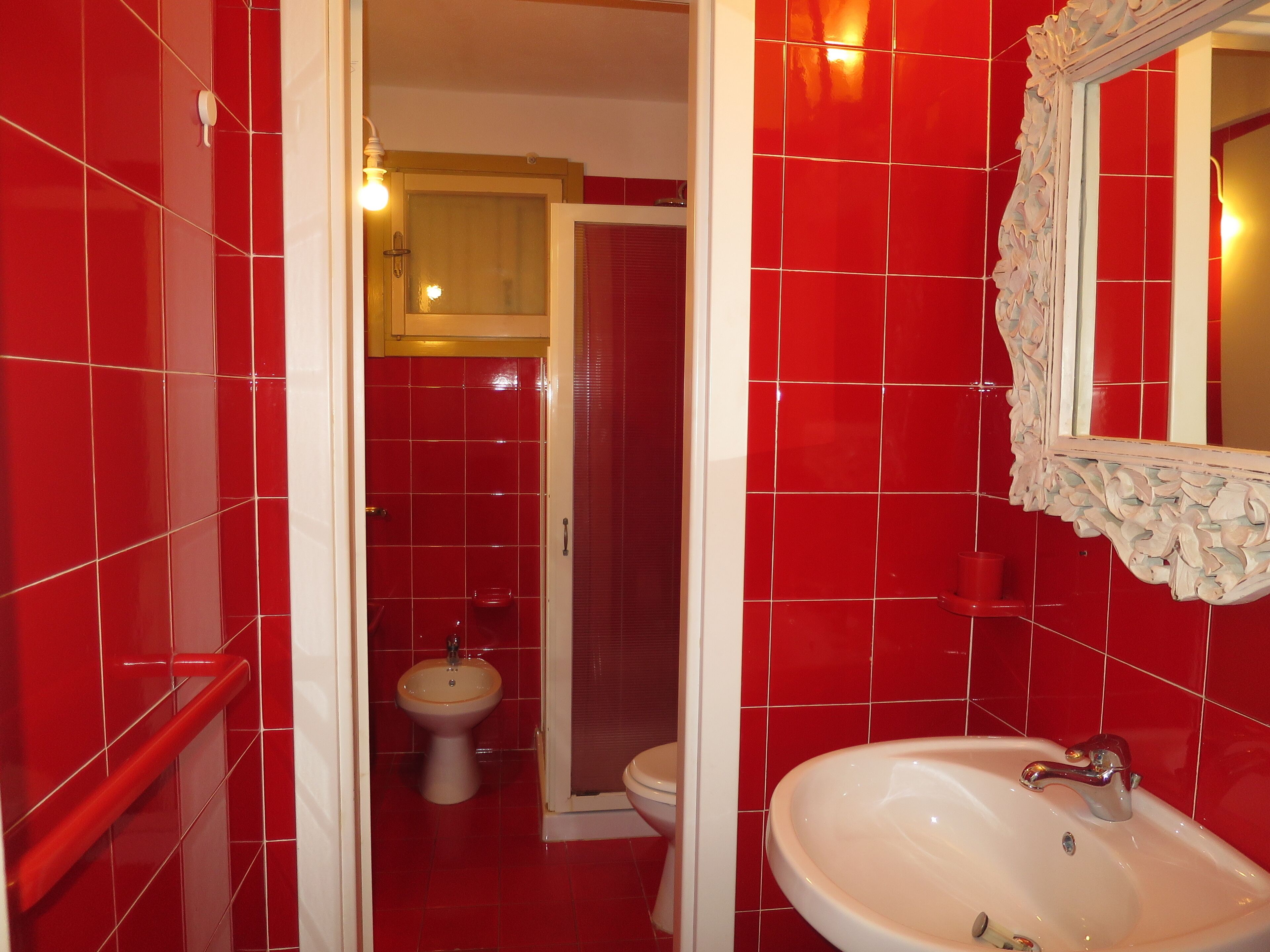 A bathroom with red tiles, a white sink, and a mirror with an ornate frame.
