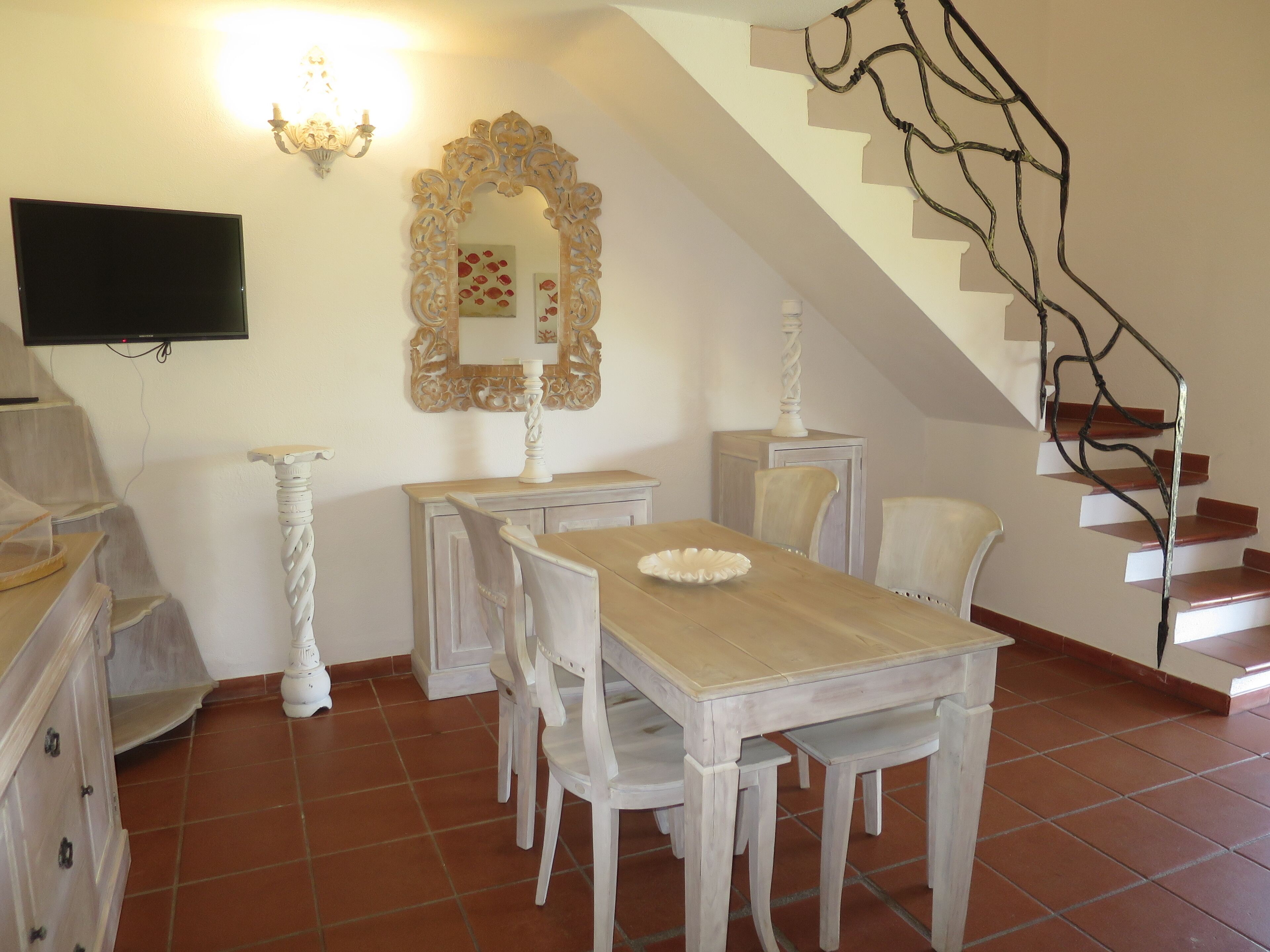A dining area with a wooden table and chairs, a decorative mirror, and a staircase.