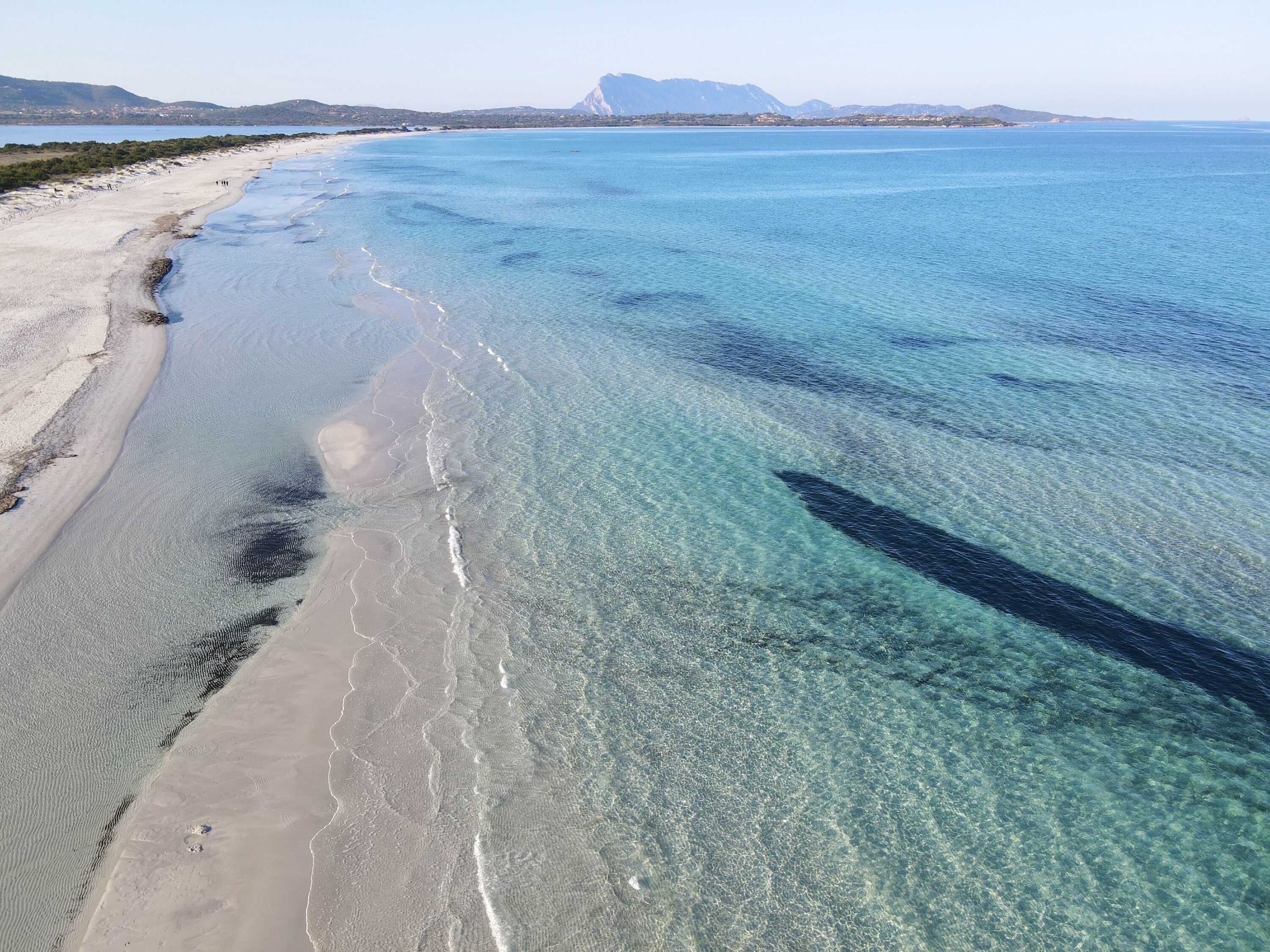 A beach with clear shallow waters and a sandy shore.