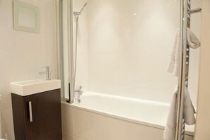 A bathroom with a bathtub, a shower, and a vanity with a mirror.