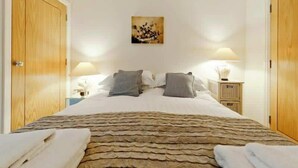 Une chambre à coucher avec une couvre-lit à motifs de pierres, deux tables de chevet avec des lampes, un tableau au mur et des portes en bois.