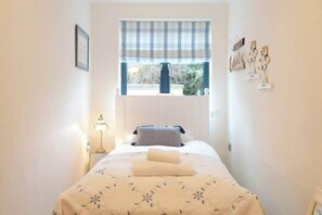 Un dormitorio pequeño con una cama, una ventana con persiana cuadriculada, una mesita de noche con lámpara y adornos en la pared.