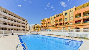 Una piscina con una escalera metálica, rodeada de edificios de varios pisos con balcones y un cielo despejado.