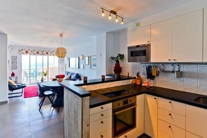 A modern kitchen with a central island, built-in oven, and white cabinetry. - Arce 2 (Nerja)