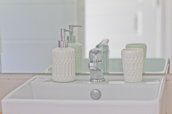 A bathroom sink with a white basin, a silver faucet, and two white soap dispensers. - "O Coeur de Deshaies", Papaya Duplex. Room with sea view. A/C, swimming pool. (Deshaies)