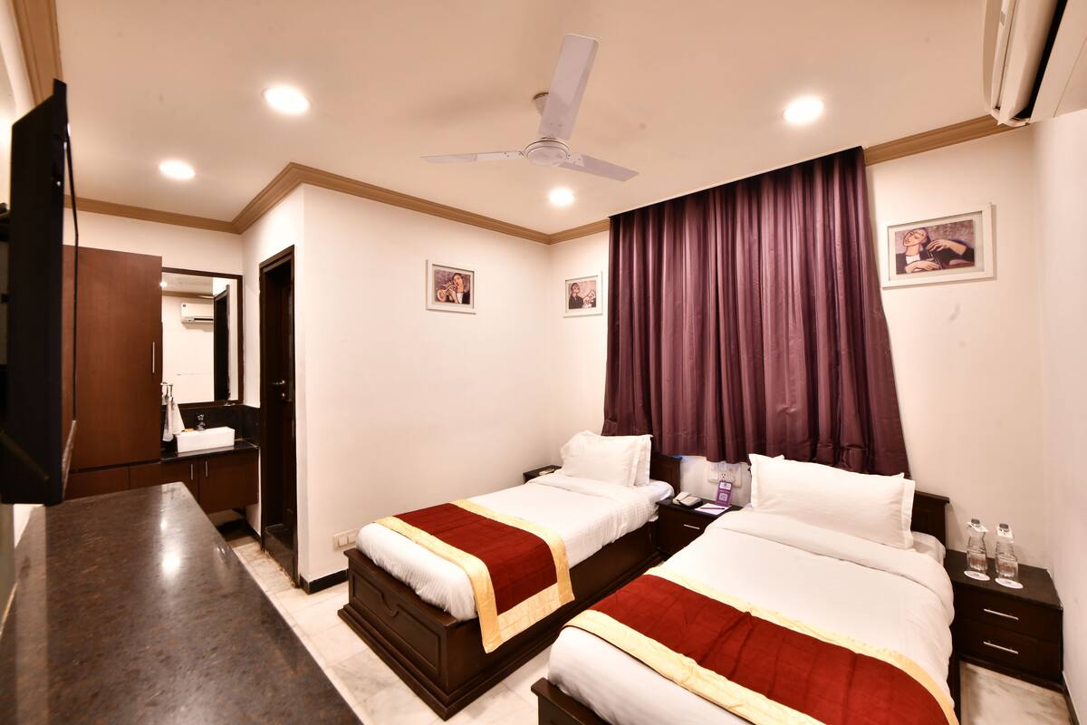 A hotel room with two beds, a flat-screen TV, a ceiling fan, and a bathroom visible through an open door.