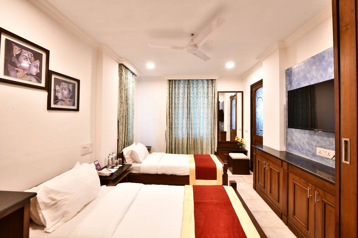 A hotel room with two beds, a TV, a wardrobe, and a ceiling fan.
