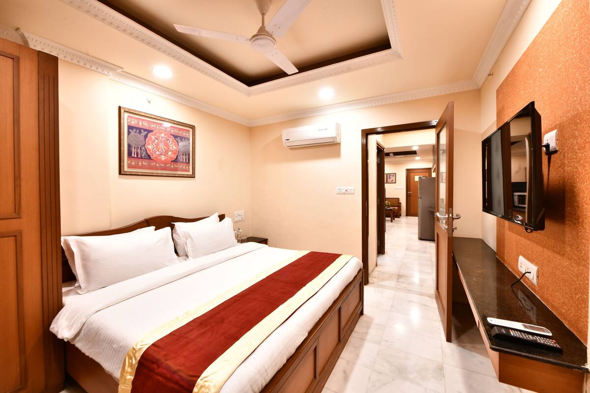 A hotel room with a bed, a TV mounted on the wall, and an air conditioning unit.