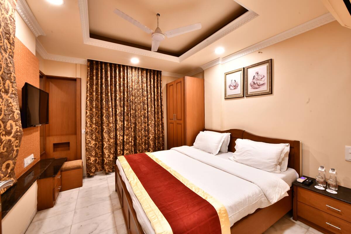 A hotel room with a bed, a nightstand, a TV, a ceiling fan, and curtains.