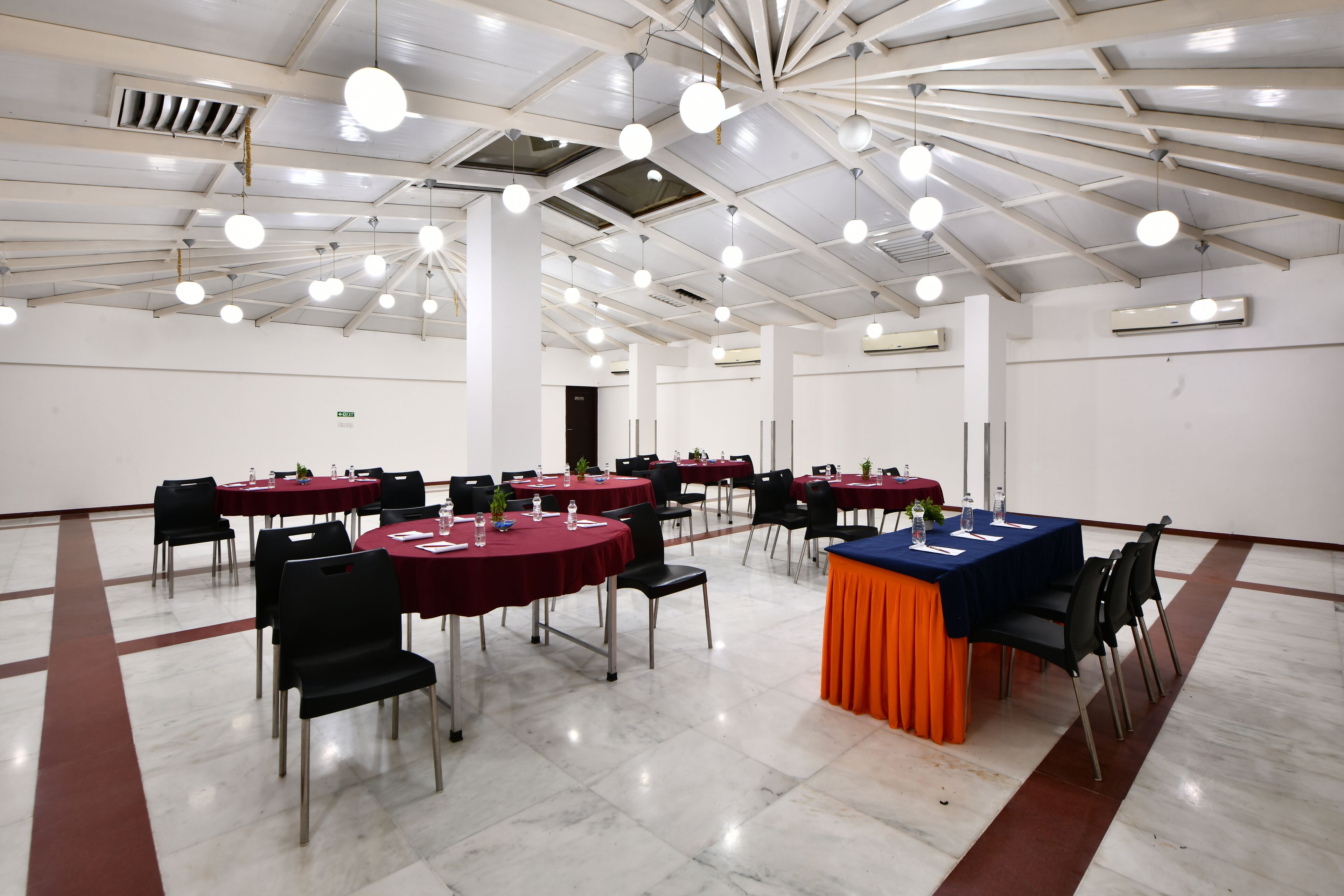 Un salón de conferencias con mesas redondas, sillas y una mesa central con mantel azul.