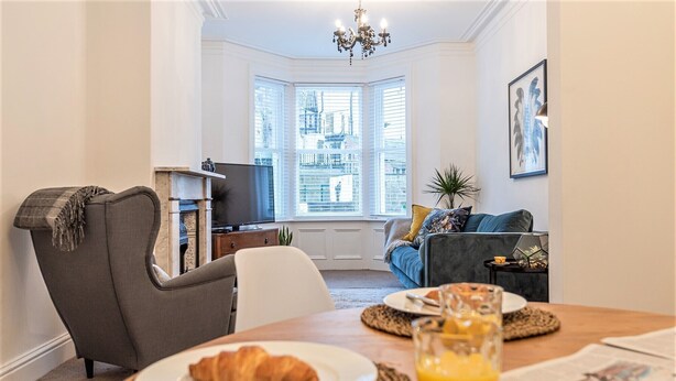 Un salon confortable avec une cheminée, un téléviseur et un coin repas où l’on trouve un croissant et du jus d’orange.